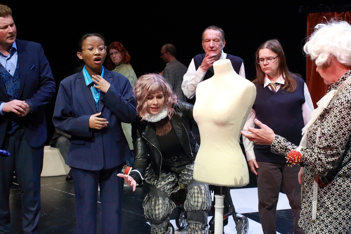 © Peter Schlipf Verschiedene Menschen stehen mit geschocktem und verwirrtem Gesichtsausdruck um eine leere Schaufensterpuppe herum