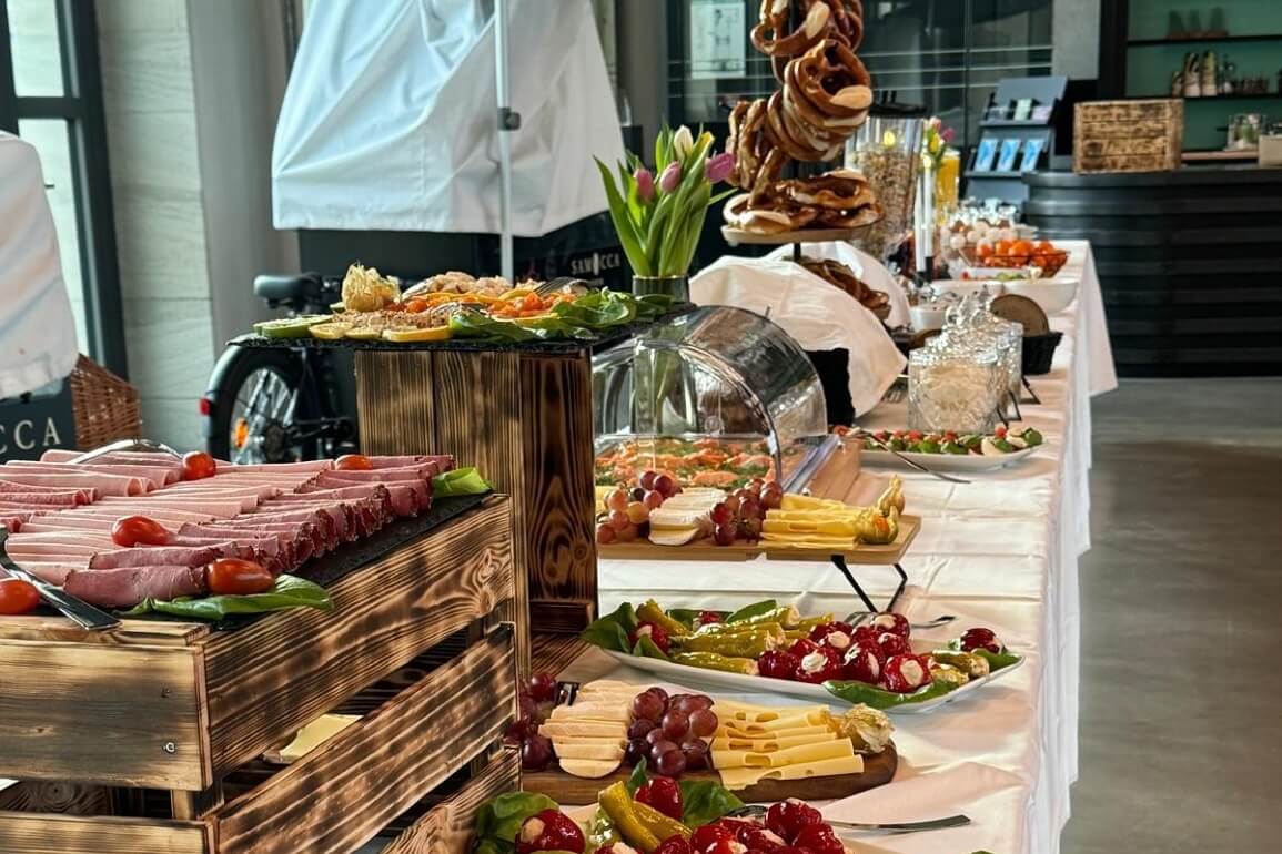 © Viktoria Junker Auf einem Tisch sind verschiedene, reichhaltige Frühstücksmöglichkeiten aufgebaut, z.B. Wurst- und Käseplatte, noch geschlossene Wärmebehälter sowie Brezeln