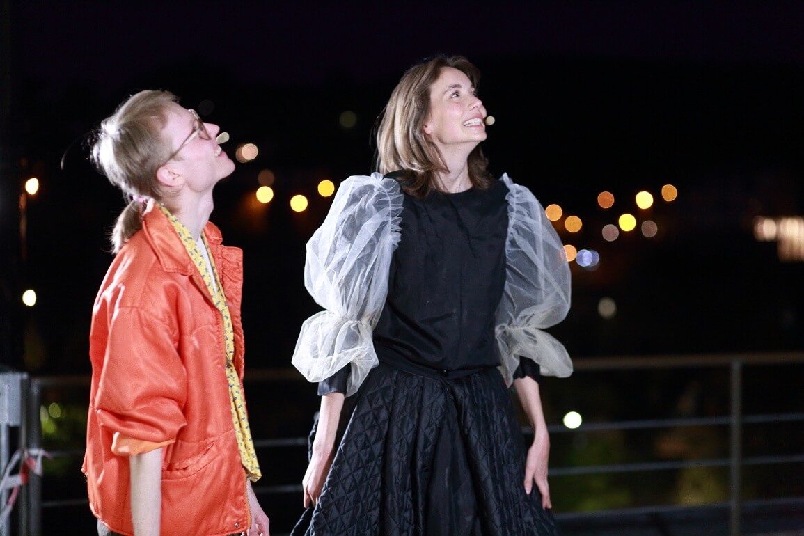 Zwei Personen stehen draußen in der Nacht nebeneinander und schauen lächelnd nach oben