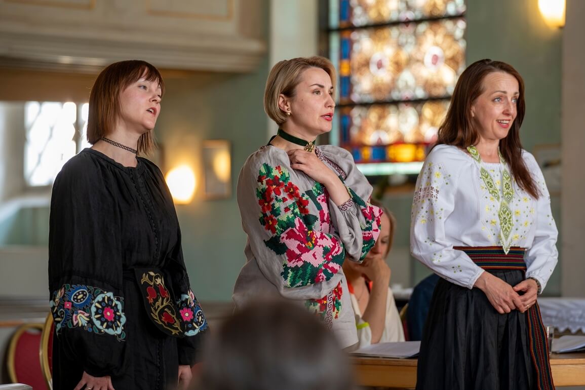 © Andreas Trunschke Drei Frauen in ukrainischer Trachtenkleidung stehen in einem sakral anmutenden Raum und singen
