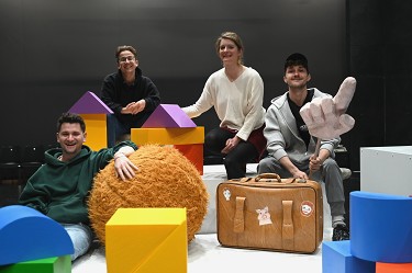 vier Personen sitzen inmitten von großen bunten Bauklötzen und lachen in die Kamera